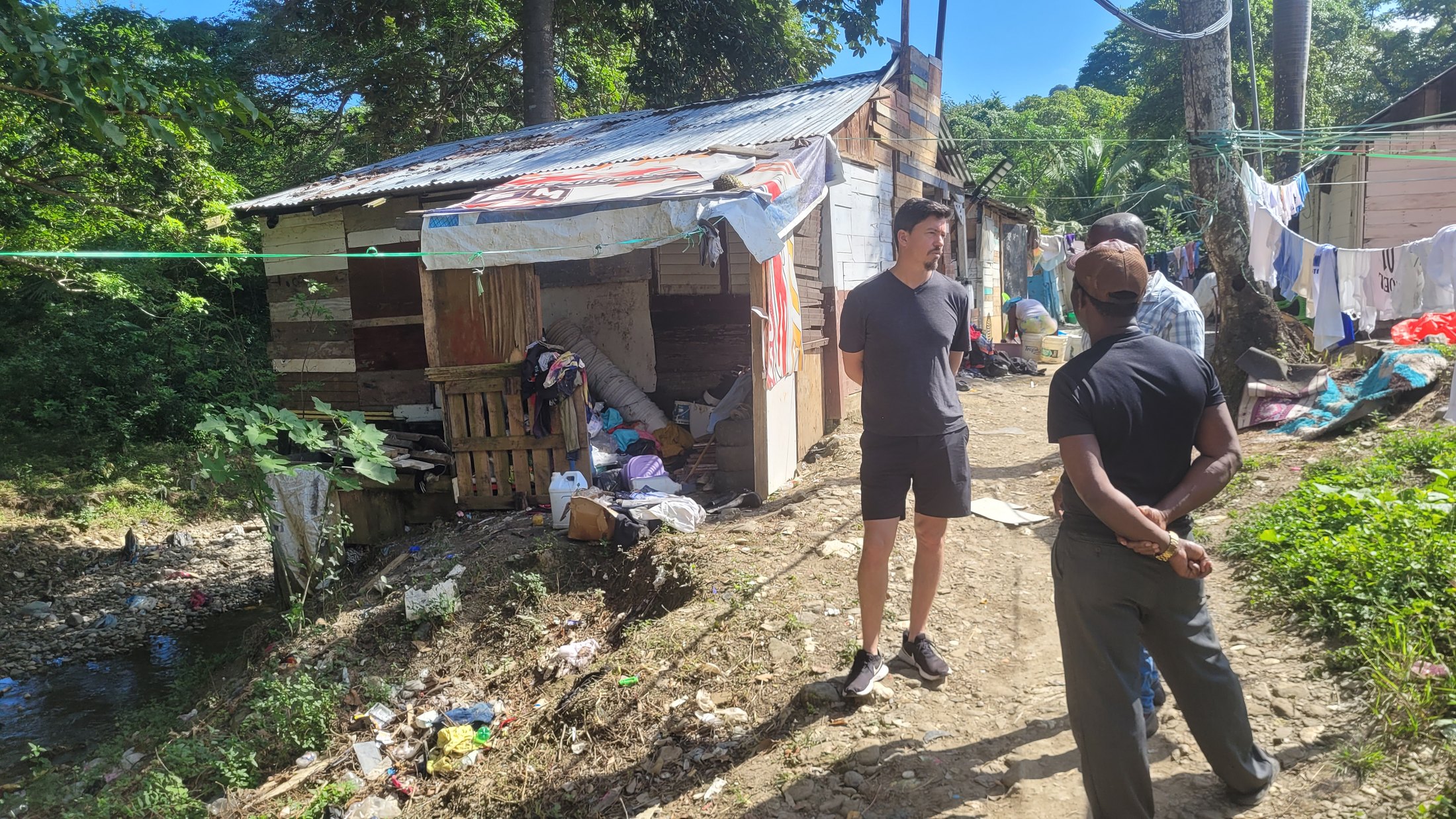 Pedro Serra speaking with two men on a dirt path beside wooden homes in the Dominican Republic