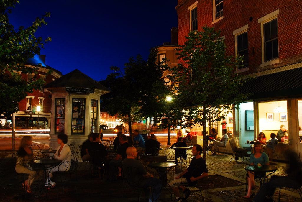 People at outdoor cafe tables on a brick street at night in Portsmouth