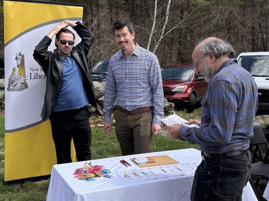 Pedro Serra at an outdoor outreach table beside a New Hampshire Liberty banner