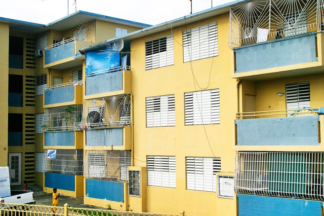 A yellow public-housing building in Puerto Rico, with barred balconies and a child in the courtyard